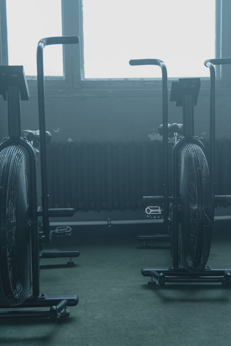 A set of exercise bikes in an empty, dimly lit gym with a muted atmosphere.